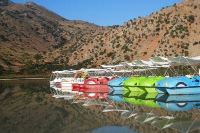 A panoramic view of Lake Kournas surrounded by hills and trees on a sunny day in Crete.