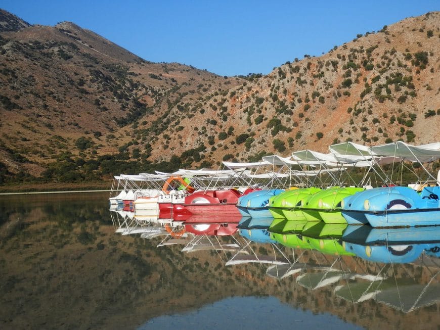 A panoramic view of Lake Kournas surrounded by hills and trees on a sunny day in Crete.